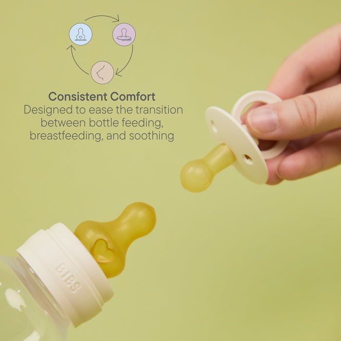 BIBS Baby Bottle Round Latex Nipple held by hand beside BIBS bottle on green background, text reads "Consistent Comfort"