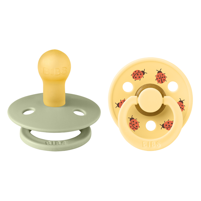 BIBS Studio Colour 2 Pack Ladybug pacifiers on white background: sage green and yellow with red ladybug print, BIBS embossed