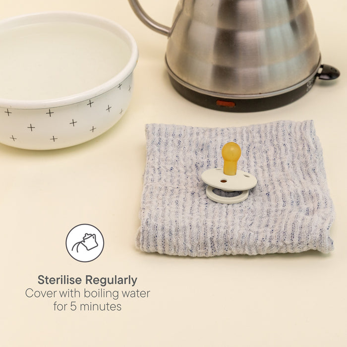 BIBS Pacifier Bumblebee latex soother on grey cloth beside bowl and kettle, cream background. Text: "Sterilise Regularly, Cover with boiling water for 5 minutes"