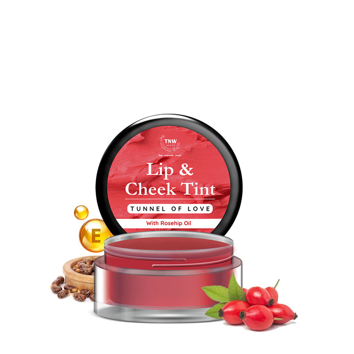 A small open jar of Lip & Cheek Tint in a red shade, labeled 'Tunnel of Love', with rosehip oil depicted next to it, andberries nearby suggesting the product's natural ingredients.
