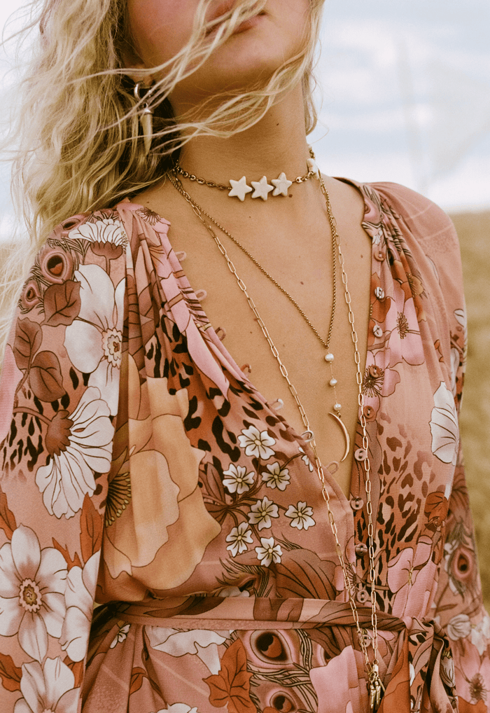 Close-up of a model wearing Stealing Beauty Gown in Rose Quartz, layered gold necklaces over floral print V-neckline